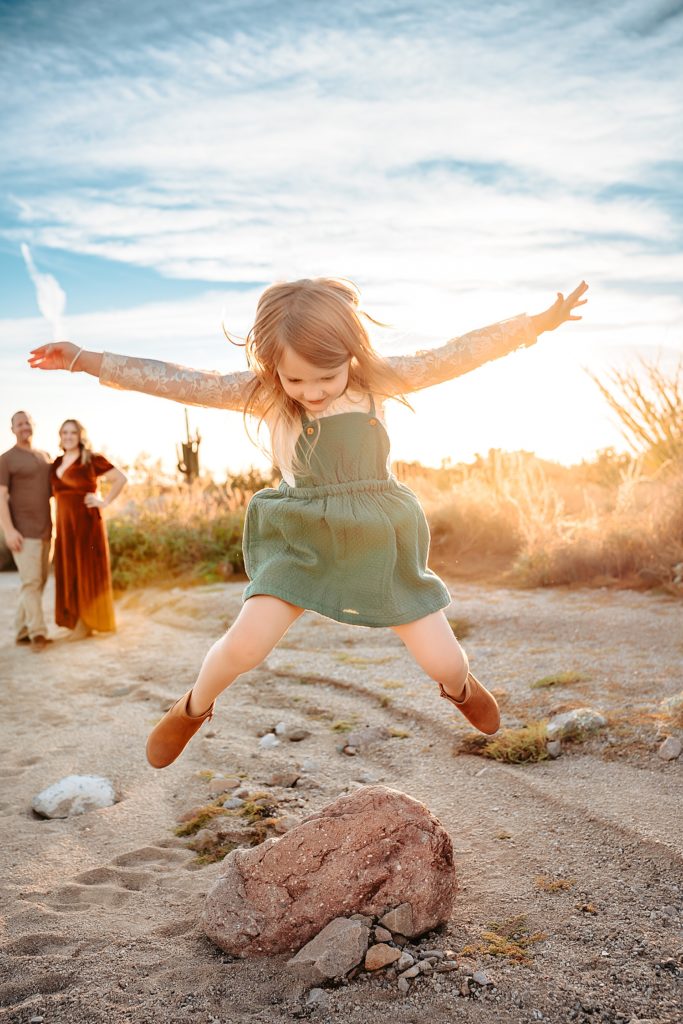 little girl jumping in mid air, with her parents watching in the background.