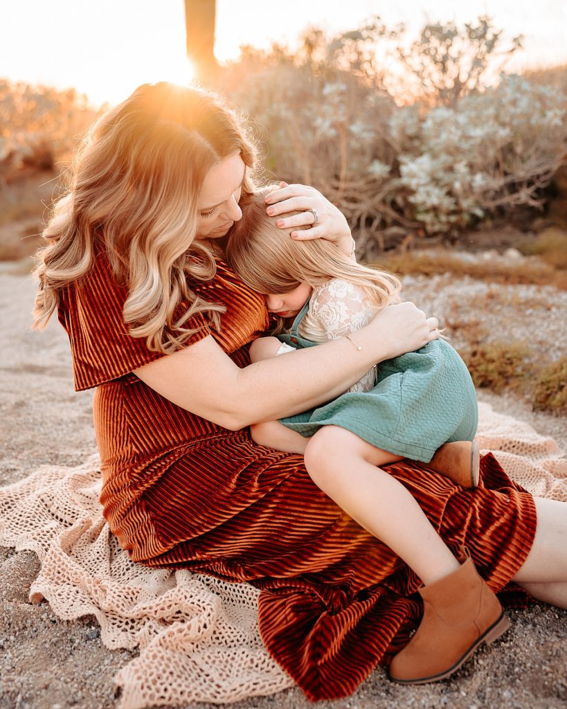 Mom in a rust colored velvet dress snuggling her little girl on her lap. 