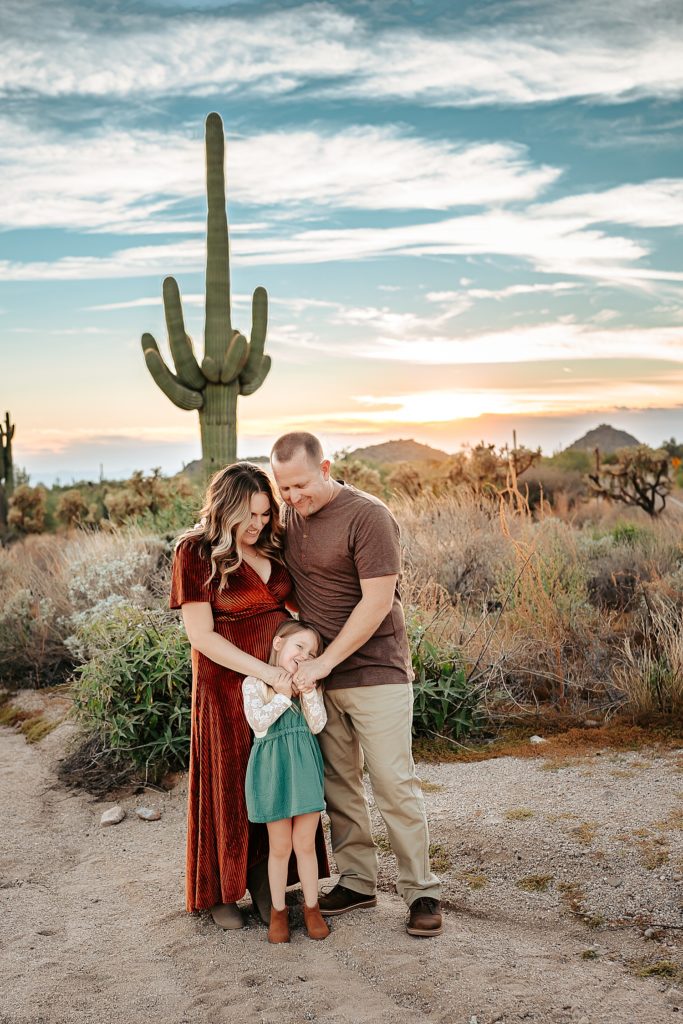 family of three standing in front of Arizona scenery in boho clothing for their family photo session. 