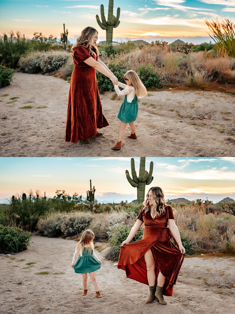 Mother in a velvet dress and daughter in a green jumper dancing together with the Arizona scenery behind them. 