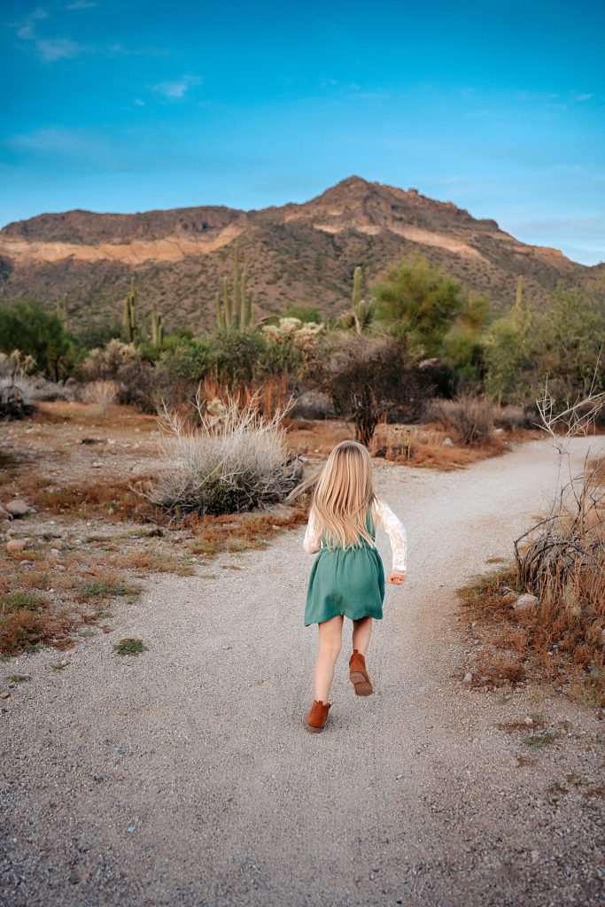 Little blonde girl running down path away from the camera towards the mountains in the background. 