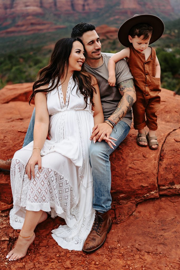 Family of three sitting on a rock for their maternity session in Sedona, Arizona