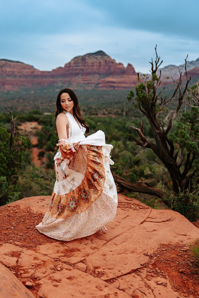 Woman in white dress spinning on top of a rustic overlook in Sedona, Arizona.