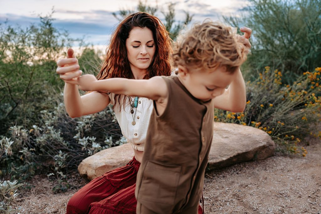 Mom holding sons hands as he takes steps at this boho family session in Arizona. 