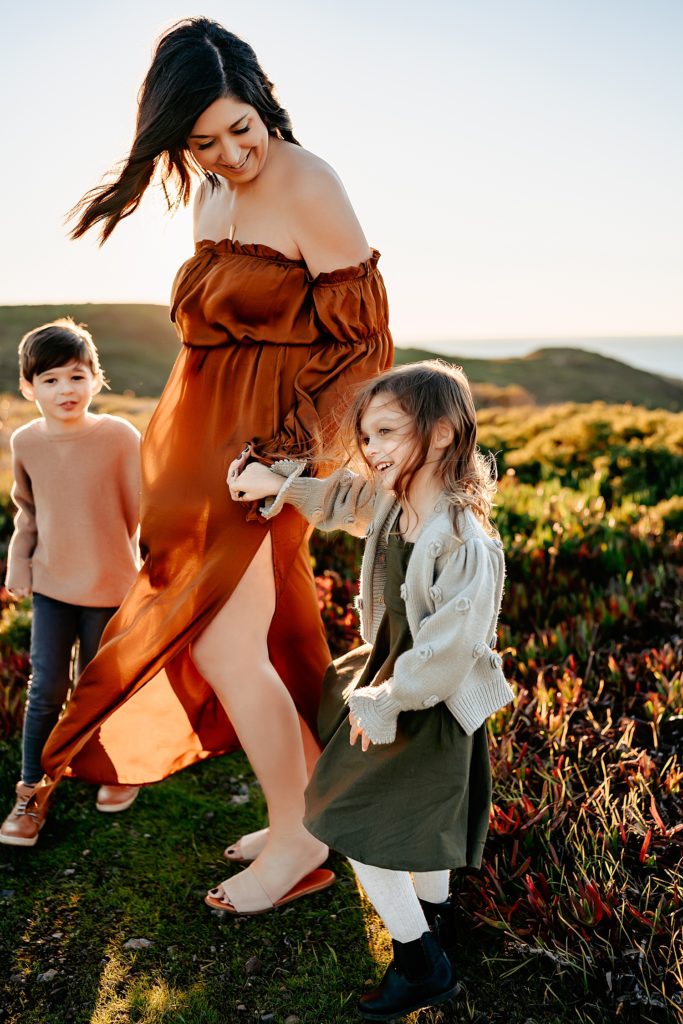 Mom in rust colored dress walking while holding her two children's hands