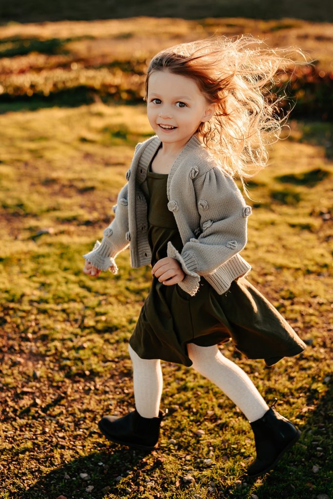 Young girl in cardigan running across a field. 