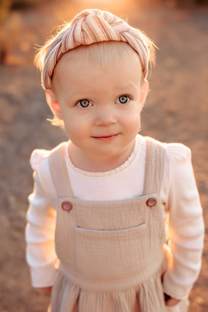 Baby girl with headband looking up into the camera wearing a linen jumper.