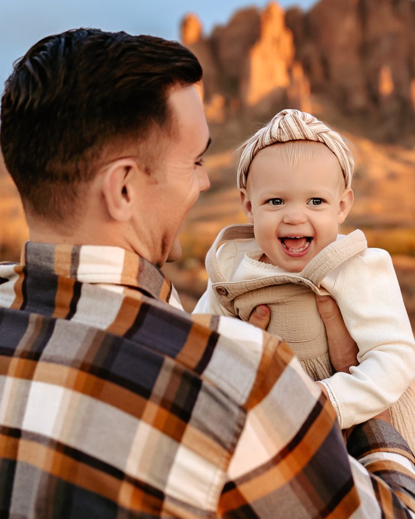 Dad in plaid holding up baby girl as she is laughing. 