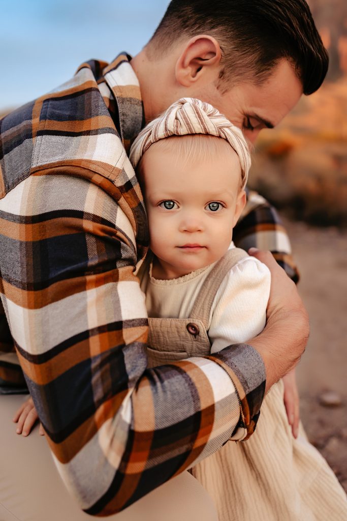 Dad holding his young girl close as she looks in to the camera for their session in Lost Dutchman State Park. 