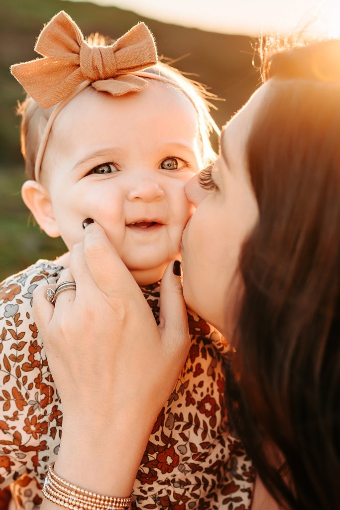 Up close of a baby's face with her mama kissing her cheek. 