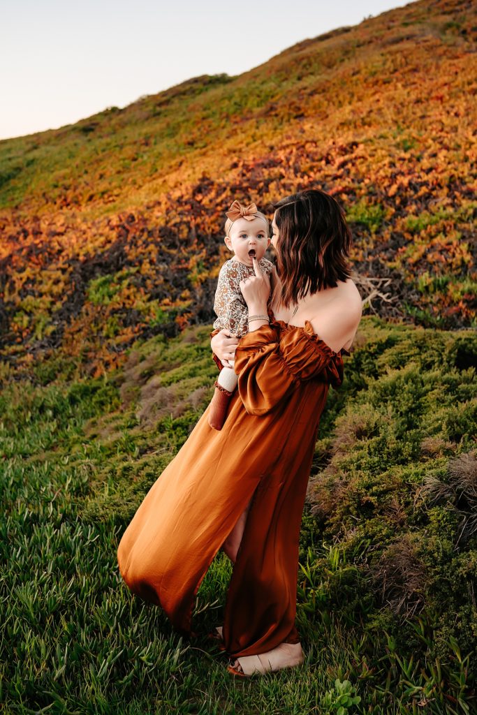 Mama in boho dress playing with her young baby in a lush field. 