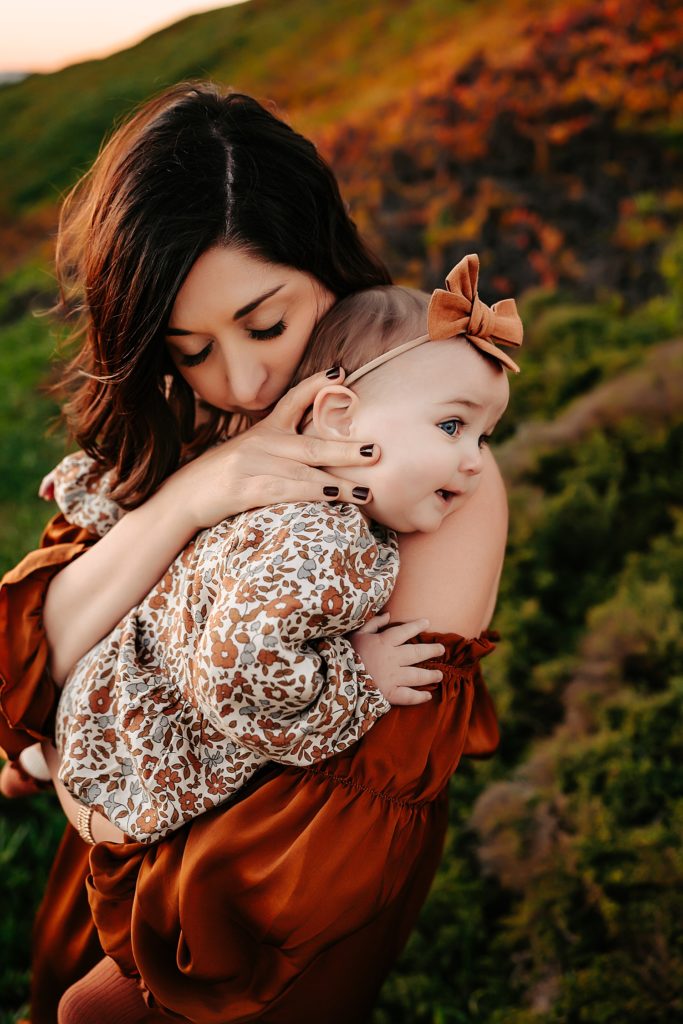 Mom in rust colored boho dress hugging her baby close. 
